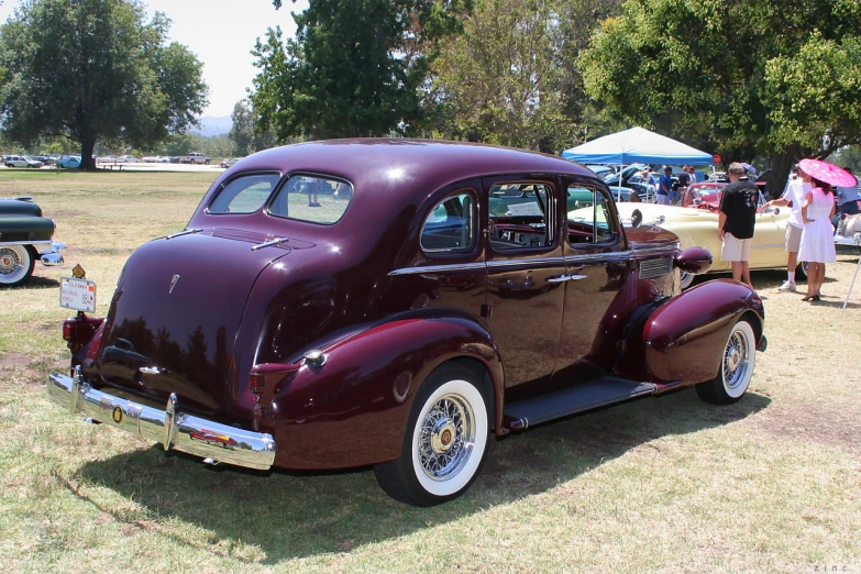 an old model car is parked by people with umbrellas