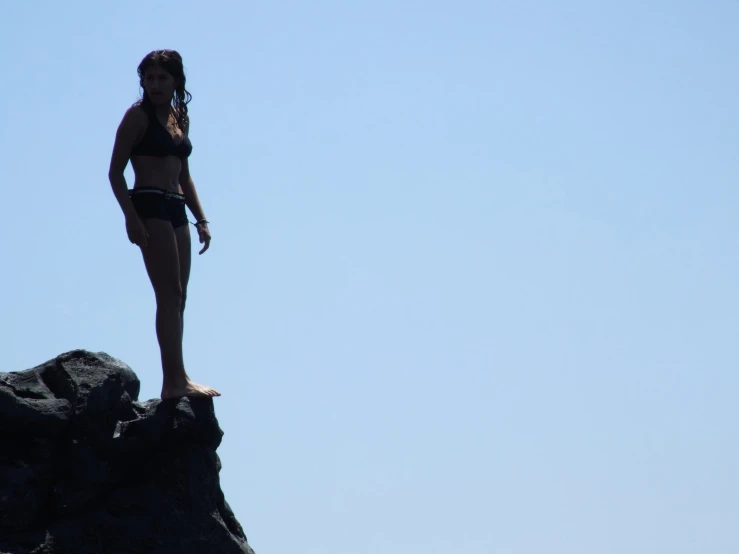 a beautiful young lady standing on top of a rock