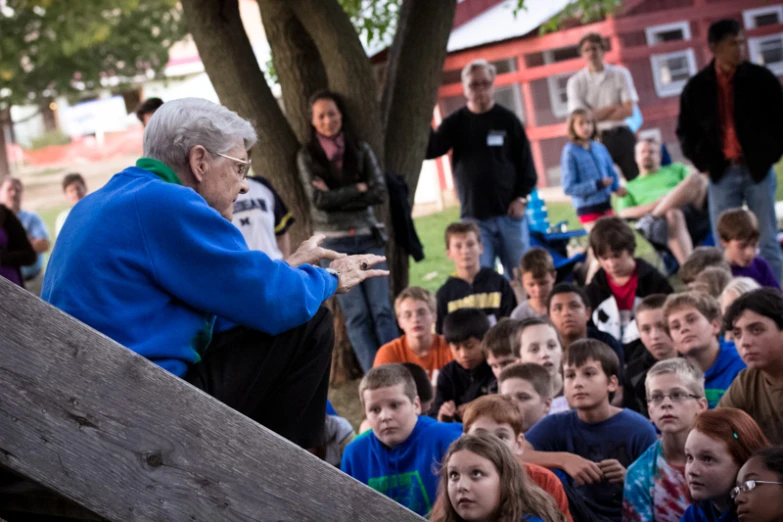 elderly lady sitting on bench addressing a crowd