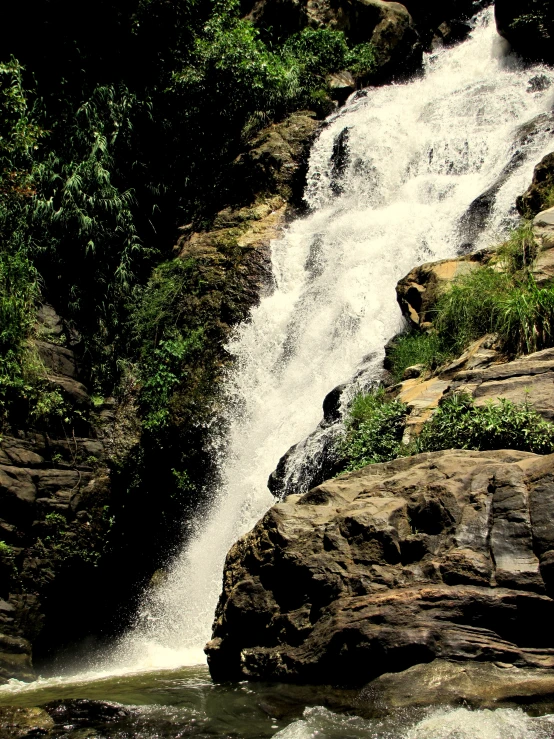 a man sitting on top of a rock near a waterfall