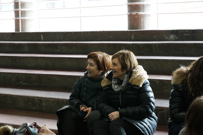 two people sitting on some steps talking and looking at each other