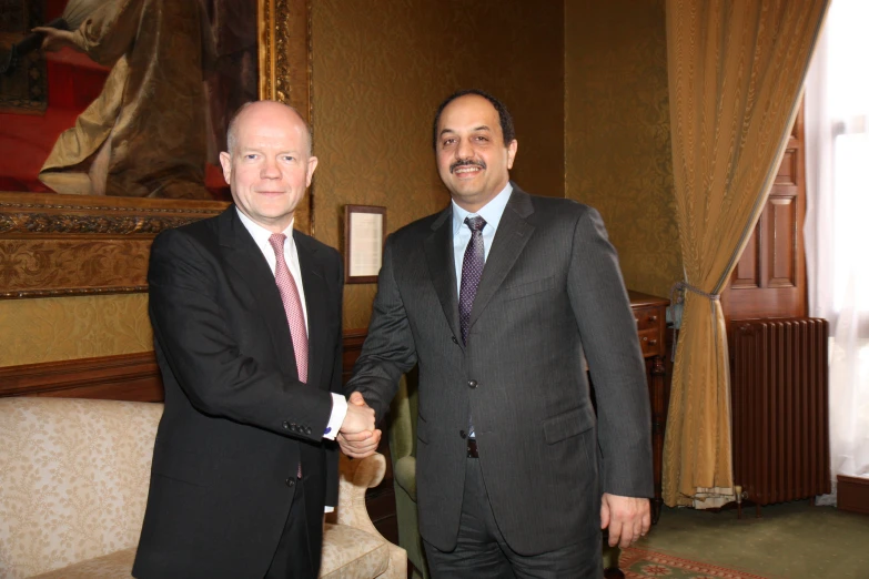 two men wearing suits shaking hands in front of a large picture