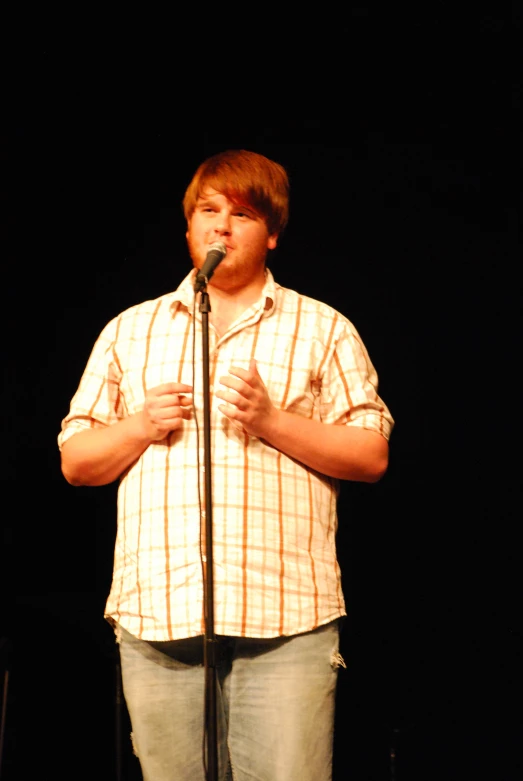 a young man standing with a microphone in front of a black background