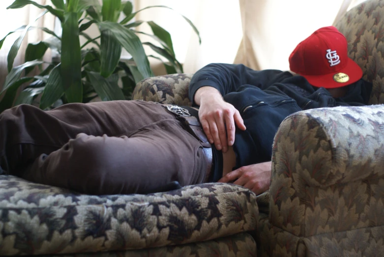 man lying on a couch wearing a hat
