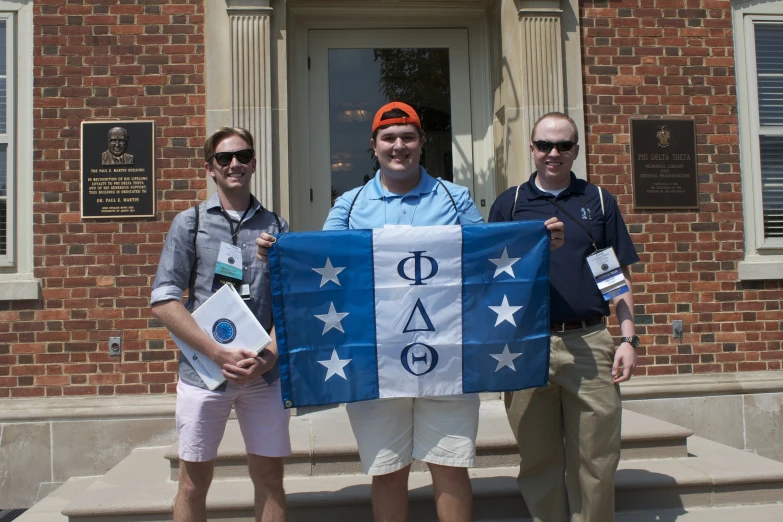 three people pose with an american flag banner in front of the building