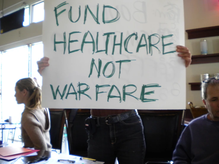 people hold a sign that reads fund healthcare not warfare