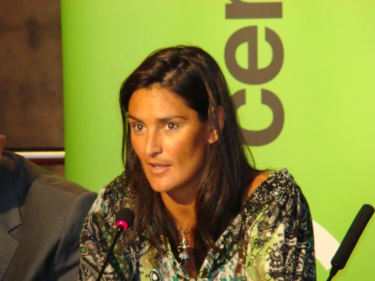 a woman sits in front of a green wall with a microphone