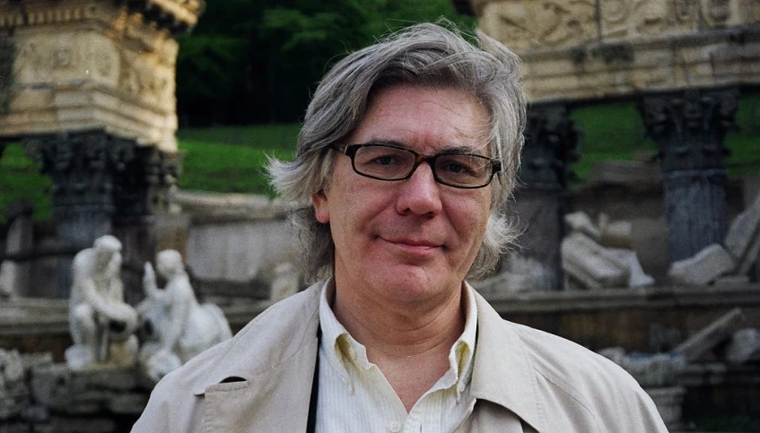 a man in glasses posing for a picture with fountains in the background