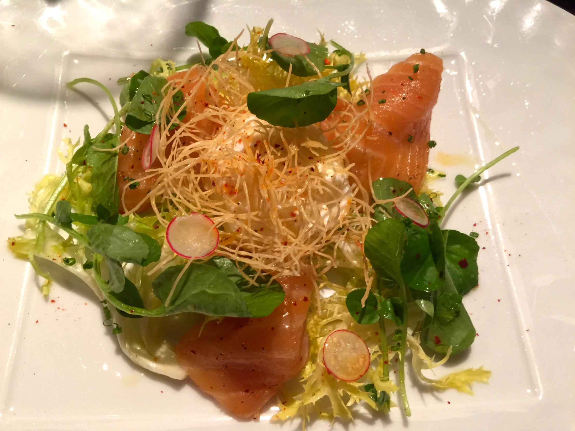 a plate filled with vegetables and fish on top of greens