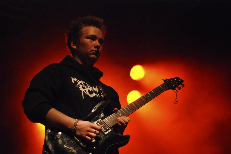 a male in black holding a guitar and playing it