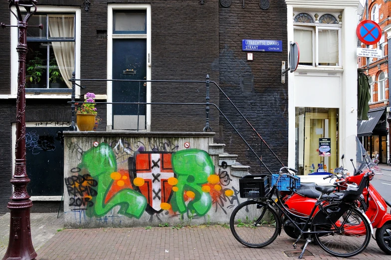 two motorcycles are parked on the sidewalk near a wall with graffiti