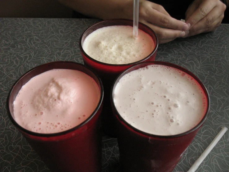 four red cups containing milk, one with straws and one has a spoon