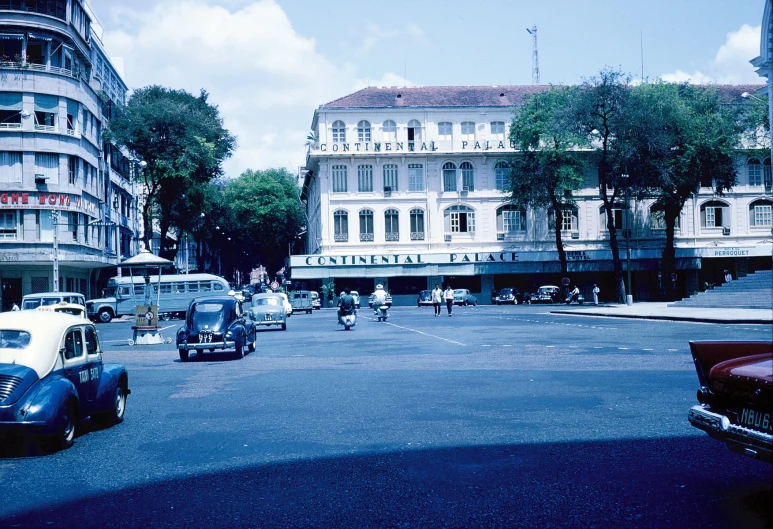 a group of cars driving down a street in front of a large white building