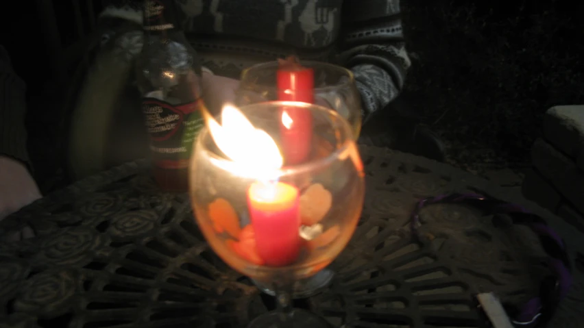 lit candle and bottle in clear glass on top of table