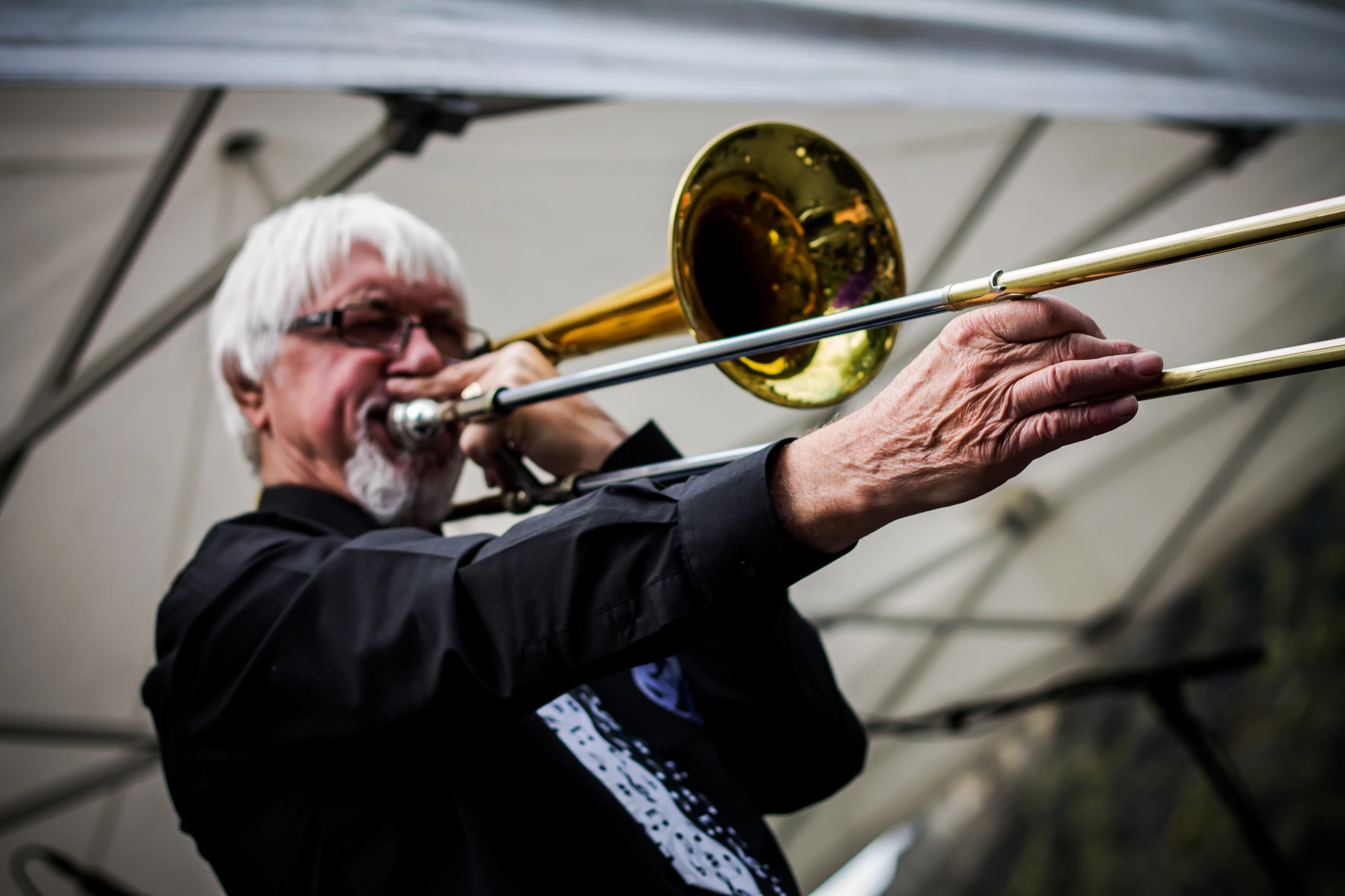 man with glasses playing trombone in front of white tents