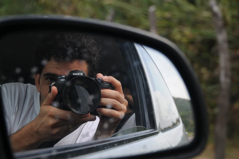 a man holding a camera takes a picture in the side mirror