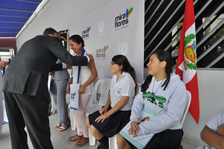 several people sitting in front of an official sign while a woman is taking pictures of them