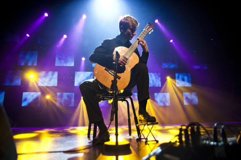 a man sitting in a chair playing an acoustic guitar