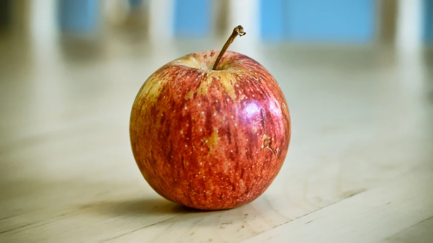 a red and yellow apple sitting on a wooden table