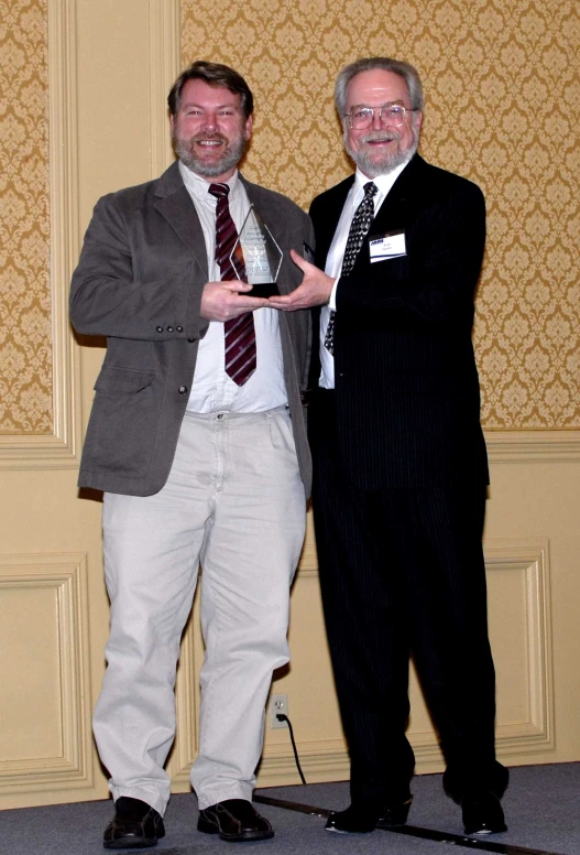 two men are standing next to each other and one is holding up his trophy