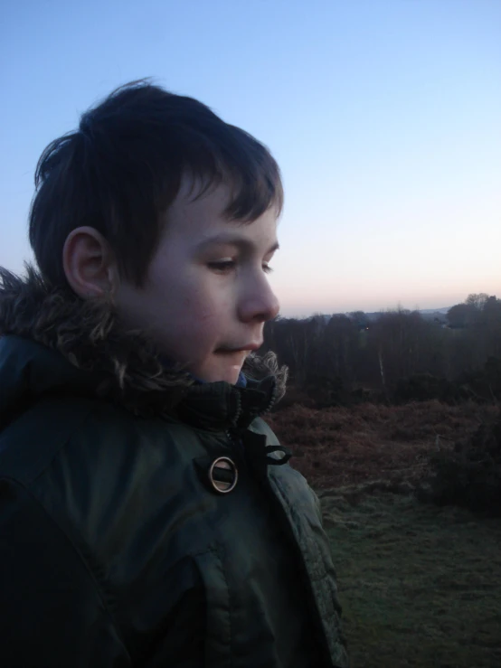 young child in black coat on open grassy field