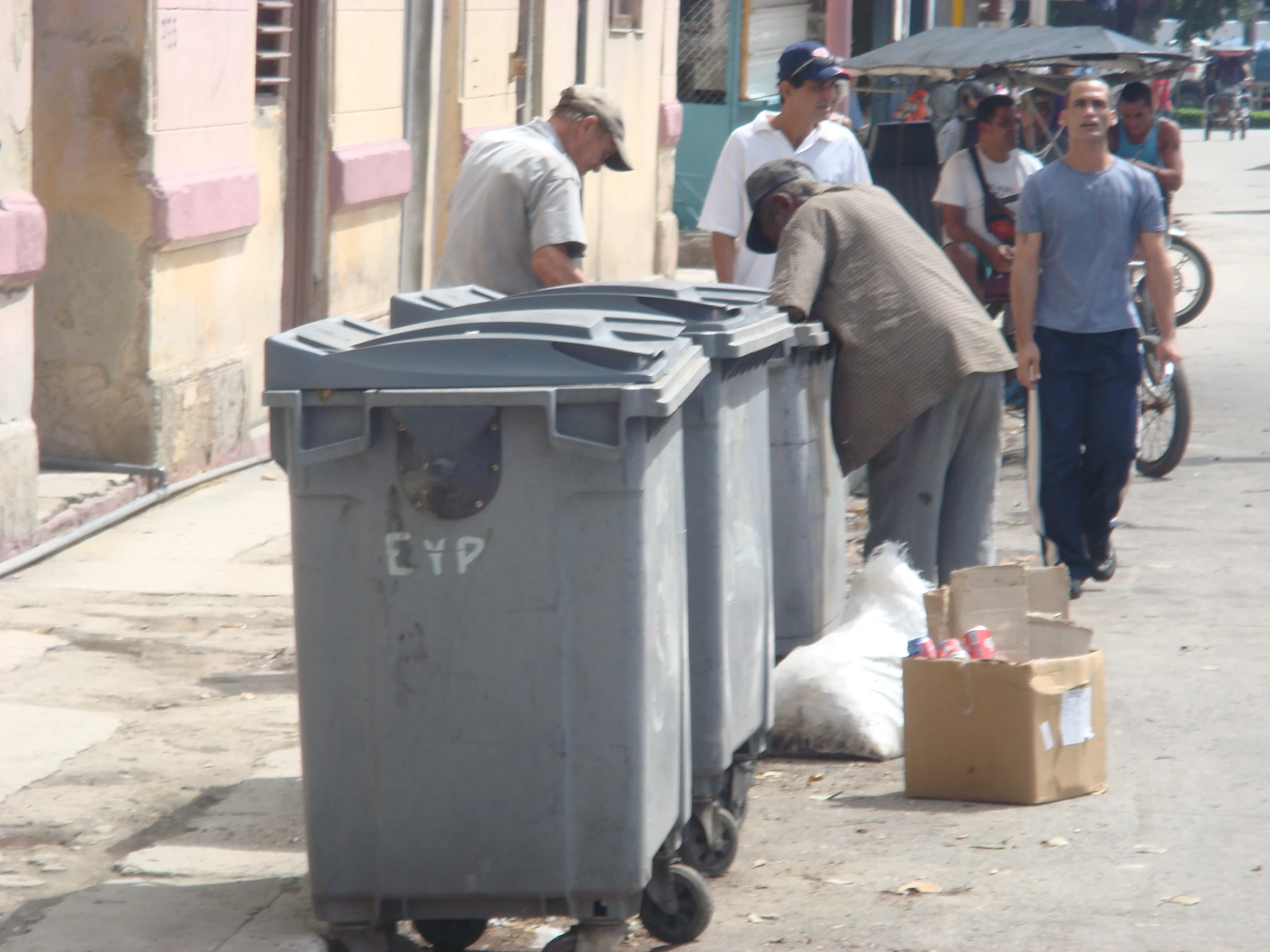 two men standing over garbage cans on a sidewalk