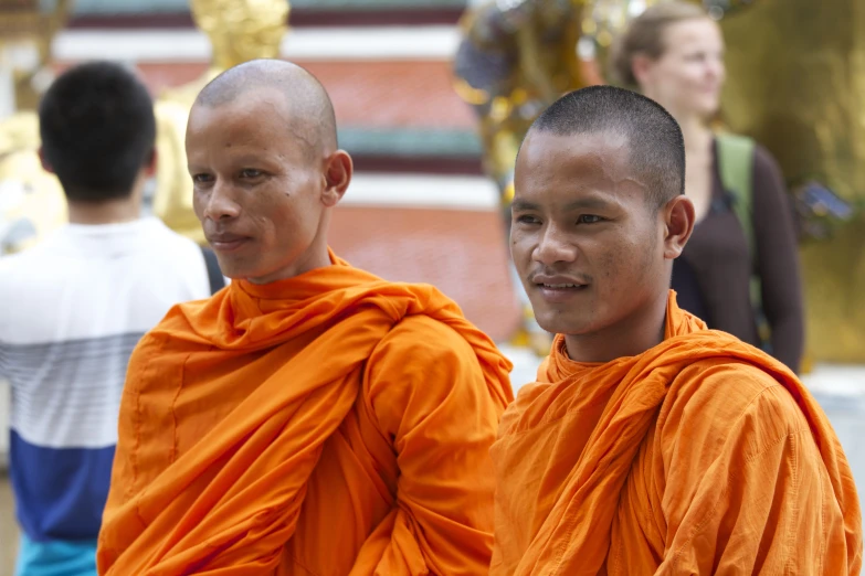 two young monks posing in front of a gold buddha statue