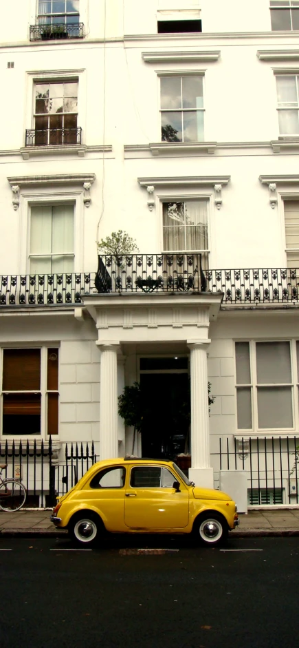 an old yellow car parked in front of a white building