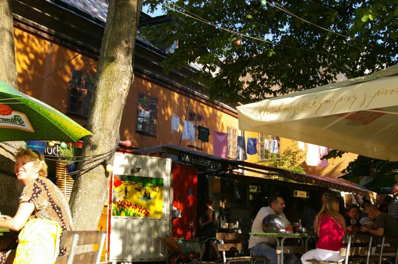 people sit at outdoor tables under an umbrella