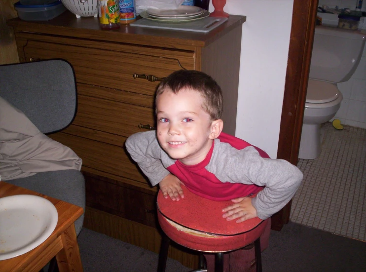 a little boy in a gray shirt sits on a stool