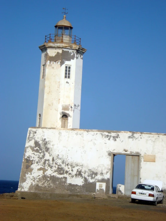 a white car sits on the side of a wall next to a light house