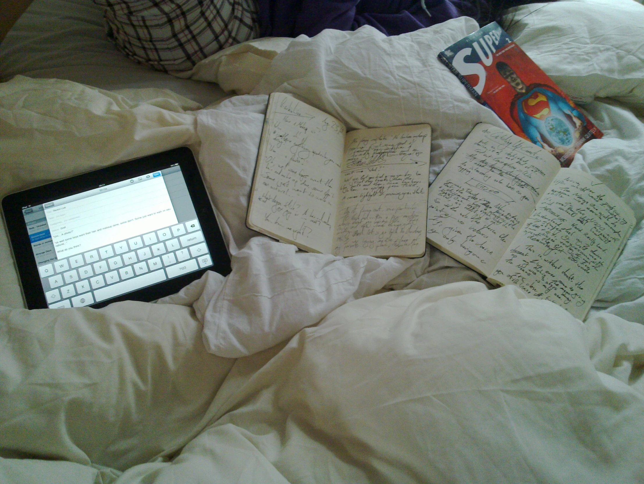 a tablet is on a bed with open notes and notebooks