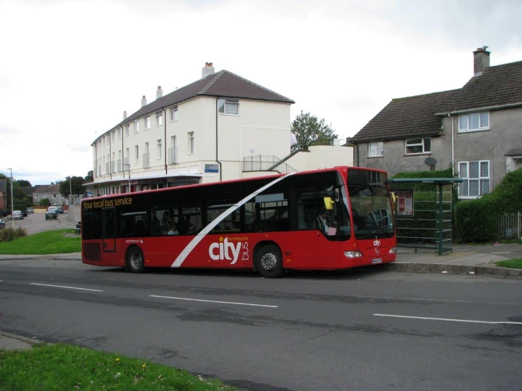 a red city bus is parked next to a green grassy field