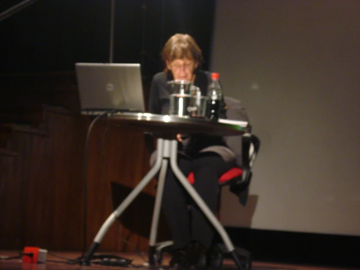 a woman sits at a table and looks at a laptop