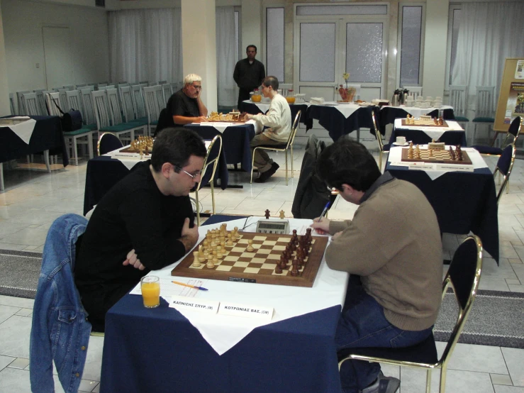 two men playing chess at a long table