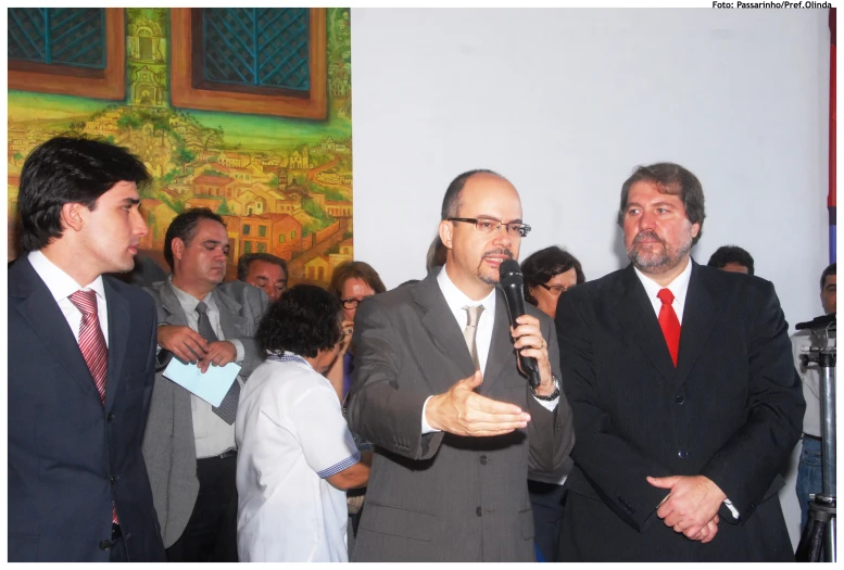 two men wearing suits talking into microphones as others watch