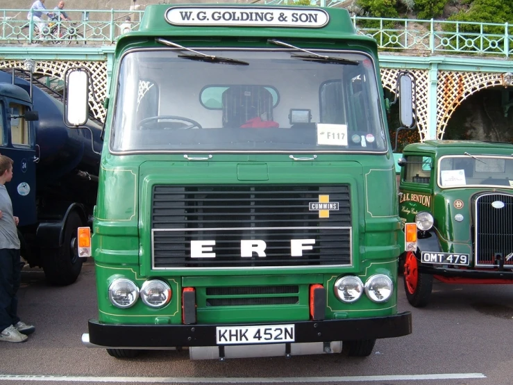 two green trucks on display next to a bridge