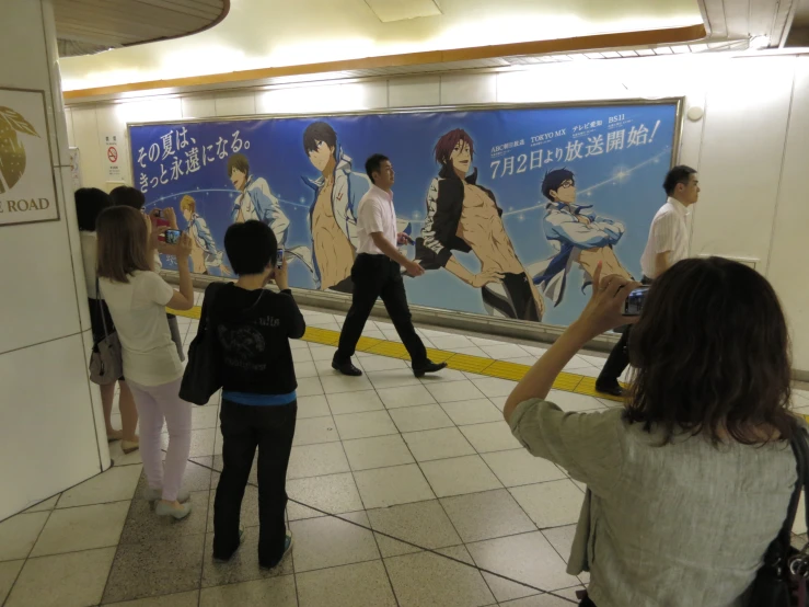 people walking by a movie poster on the wall