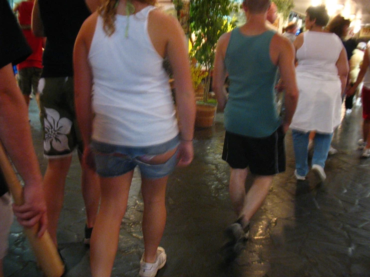 people walking down an indoor walkway lined with potted plants