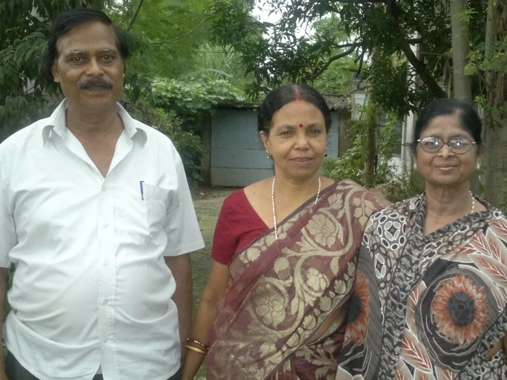 two ladies and a man standing next to each other in front of a tree