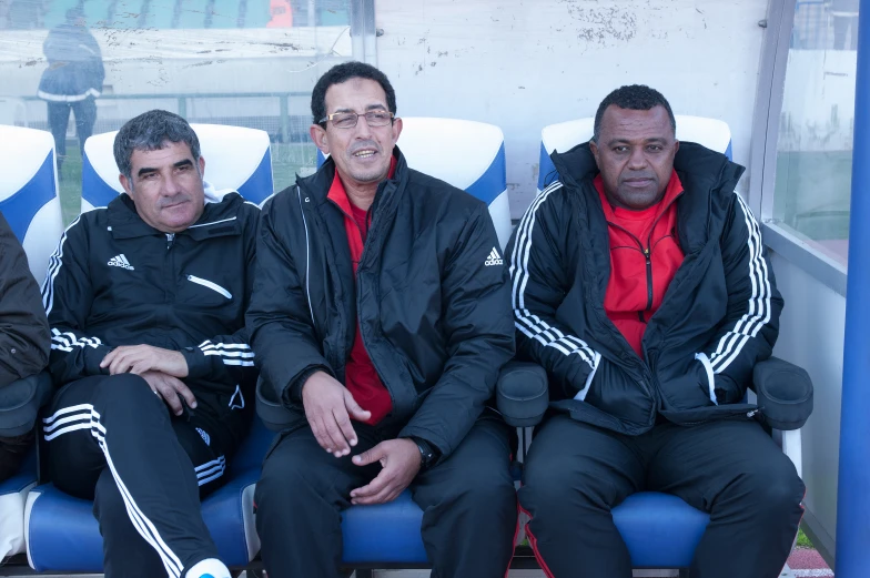 three men sit on benches at an open air stadium