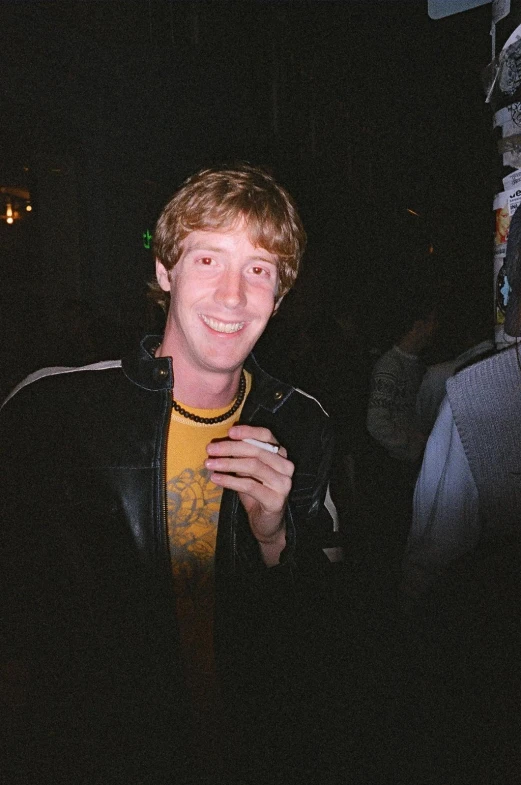a man wearing a yellow shirt and black jacket smiling