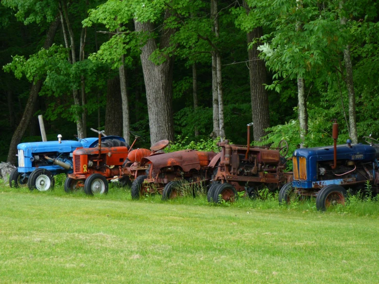 several antique farm tractors sit abandoned by a field of grass