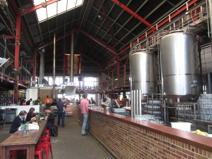 people eating at tables inside a brewery next to tall, stainless steel tanks