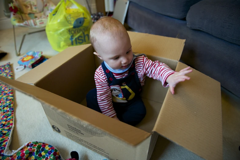 a baby wearing a bib and holding on to a cardboard box