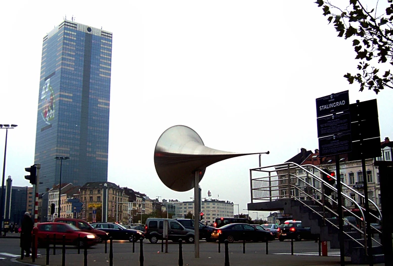 an art sculpture by a street in front of a tall building