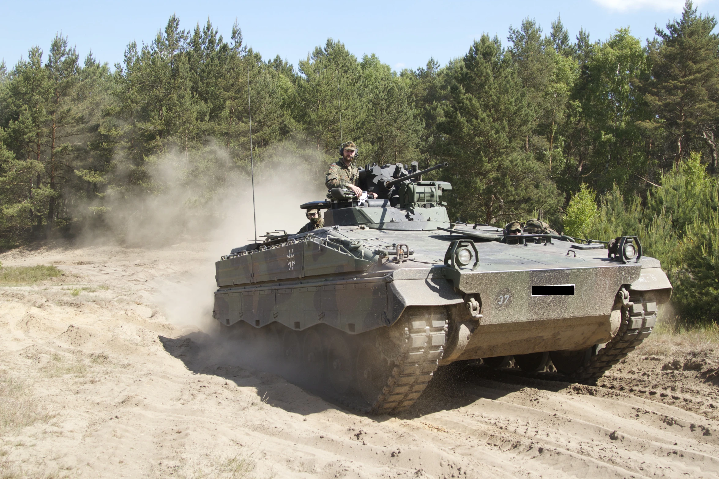 a military vehicle drives on a dusty trail