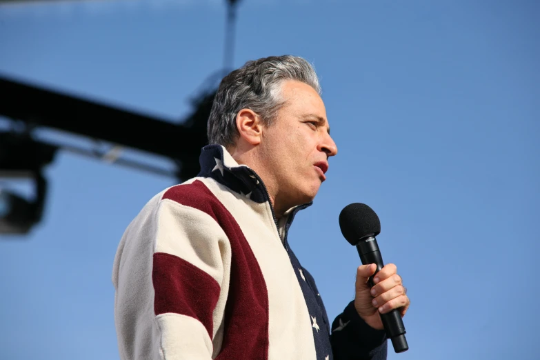 a man wearing a sweater speaking into a microphone