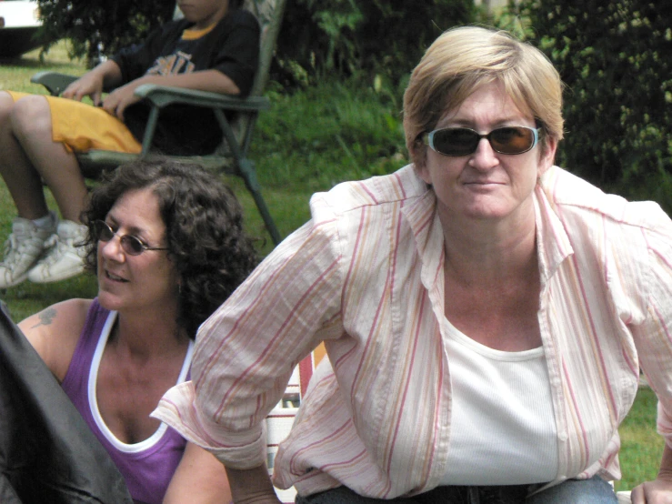 a woman wearing sunglasses and a shirt is leaning on another women shoulder