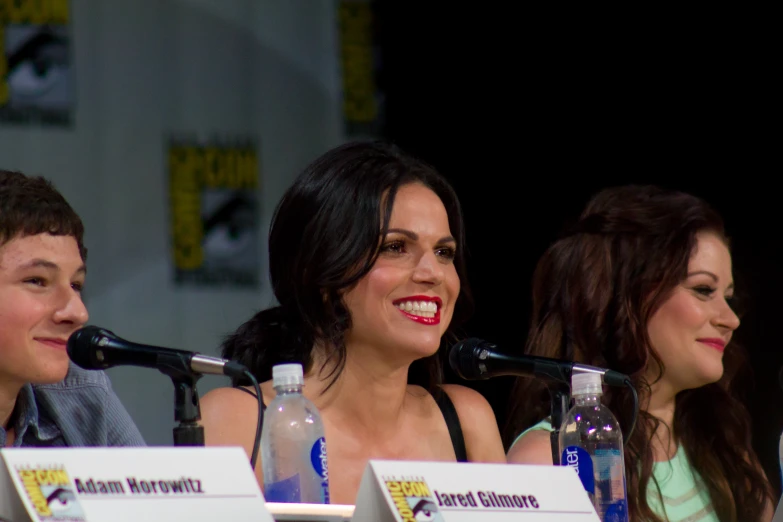 two women and a man smiling while sitting in front of microphones